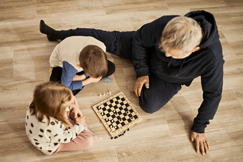 Sibling playing chess sitting with grandfather at home - ZEDF04359