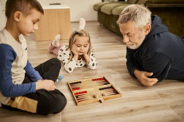 Junge und Mädchen spielen Backgammon mit ihrem Großvater zu Hause - ZEDF04368
