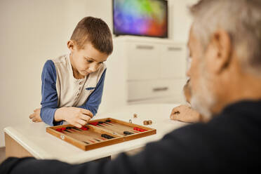 Konzentrierter Junge spielt Backgammon mit seinem Großvater zu Hause - ZEDF04375
