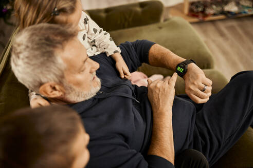 Grandfather showing time on smart watch to boy and girl sitting at home - ZEDF04379