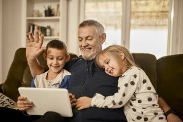 Grandchildren using tablet PC with grandfather at home - ZEDF04388