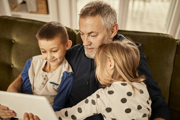 Grandchildren sitting with grandfather using tablet PC at home - ZEDF04389