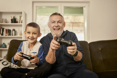 Playful grandfather playing video game with grandson at home - ZEDF04391