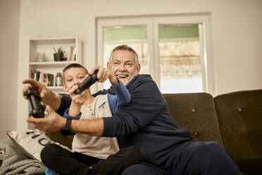 Grandfather and grandson enjoying playing video game at home - ZEDF04392