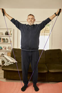 Senior man exercising with resistance band at home - ZEDF04403