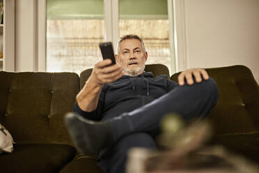 Älterer Mann mit Fernbedienung beim Fernsehen zu Hause - ZEDF04416