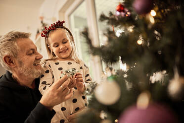 Grandfather and granddaughter decorating christmas tree at home - ZEDF04418