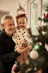 Grandfather giving gift to granddaughter on christmas at home - ZEDF04420