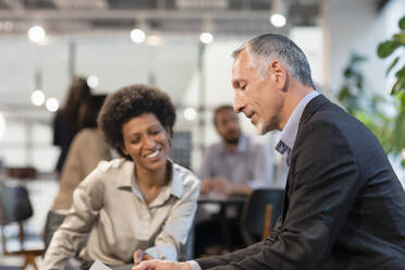 Businessman discussing with smiling colleague in office - EIF02932