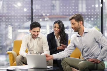 Smiling business colleagues discussing over laptop at office - EIF02940