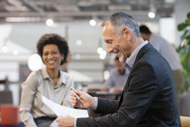 Smiling businessman discussing with colleague in office - EIF02959