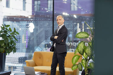 Businessman with arms crossed in office lobby - EIF02969