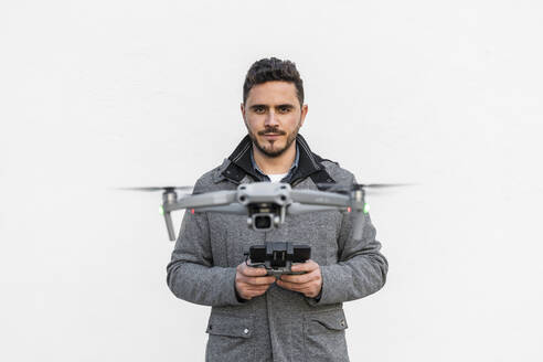Selbstbewusster Mann, der eine Drohne vor weißem Hintergrund fliegt - DLTSF02580