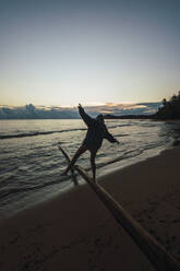 Frau balanciert auf einem Baumstamm am Strand von Limon, Costa Rica - RSGF00801