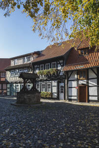 Deutschland, Sachsen-Anhalt, Wernigerode, Fachwerkhäuser entlang einer Kopfsteinpflasterstraße mit Brunnen im Vordergrund - ASCF01622