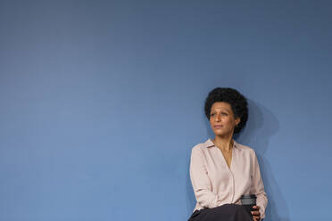 Nachdenkliche Geschäftsfrau mit Einweg-Kaffeebecher vor blauer Wand - EIF03043