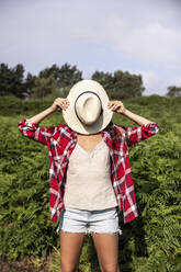 Woman covering face with hat standing in forest at Cannock Chase - WPEF05644