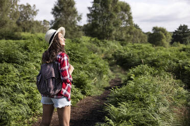 Woman with backpack standing in forest at Cannock Chase on sunny day - WPEF05646