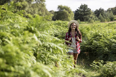 Lächelnde Frau, die an einem sonnigen Tag inmitten von Grünpflanzen in Cannock Chase spazieren geht - WPEF05648