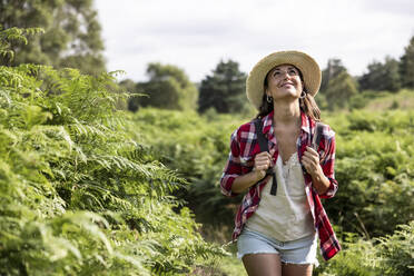 Smiling woman looking up walking in forest at Cannock Chase on sunny day - WPEF05649