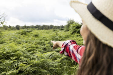 Frau mit Hut, die auf Grünpflanzen in Cannock Chase zeigt - WPEF05665