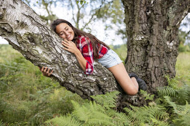 Smiling woman relaxing on tree branch in forest at Cannock Chase - WPEF05670