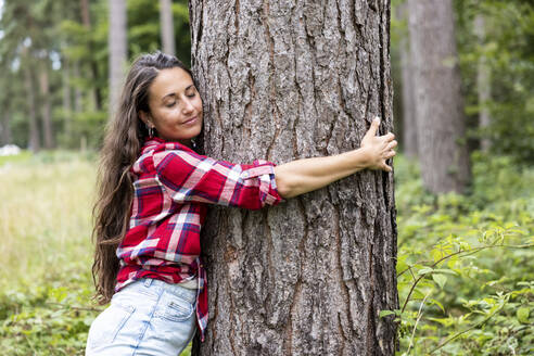 Frau mit geschlossenen Augen umarmt Baum im Wald von Cannock Chase - WPEF05673