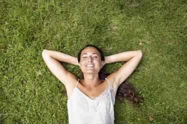 Smiling woman with hands behind head lying on grass - WPEF05688