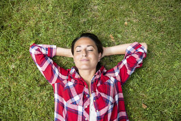 Woman relaxing on grass with eyes closed and hands behind head - WPEF05690