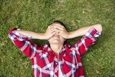 Woman covering eyes with hands lying on grass - WPEF05691