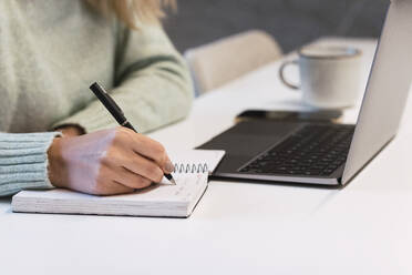 Businesswoman writing in diary at desk in studio - PNAF02769
