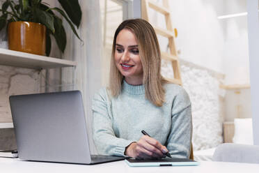 Geschäftsfrau mit Grafiktablett und Blick auf Laptop im Studio - PNAF02777