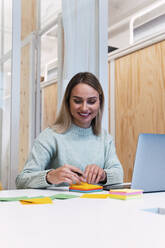 Working woman using sticky notes on desk at studio - PNAF02783