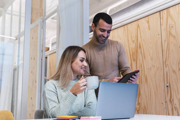 Geschäftsfrau mit Tasse in der Hand und Kollege mit Tablet-PC im Studio - PNAF02788