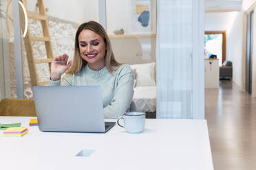 Businesswoman waving on video call at laptop in studio - PNAF02792