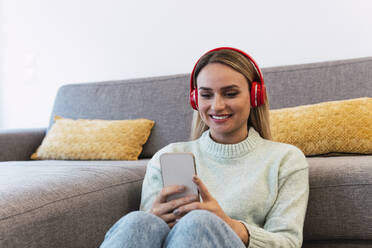 Woman listening music on headphones sitting at home - PNAF02806