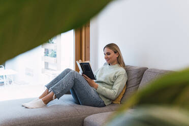 Frau liest ein Buch auf dem Sofa zu Hause - PNAF02813