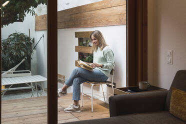 Frau liest ein Buch auf einem Stuhl im Innenhof - PNAF02816
