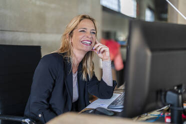 Happy businesswoman sitting at office desk - DLTSF02592