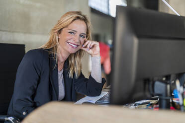 Smiling businesswoman leaning on hand at desk in office - DLTSF02594