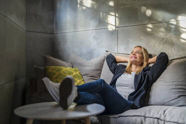 Businesswoman relaxing with hands behind head on sofa at office - DLTSF02595
