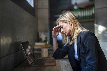 Tired businesswoman sitting with laptop on desk at office - DLTSF02603