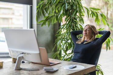 Businesswoman relaxing hands behind head at office - DLTSF02615