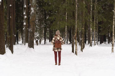 Frau mit Rucksack steht auf Schnee im Winterwald - SSGF00375