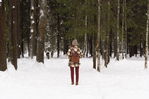 Woman with backpack standing on snow in winter forest - SSGF00375