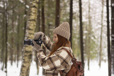 Frau beim Fotografieren mit Kamera im Wald im Winterurlaub - SSGF00377