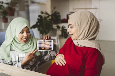 Frau zeigt Ultraschall auf schwangere Freundin im Wohnzimmer - JCCMF05089
