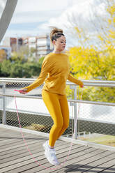 Determined young athlete exercising with jumping rope on bridge - PGF00995