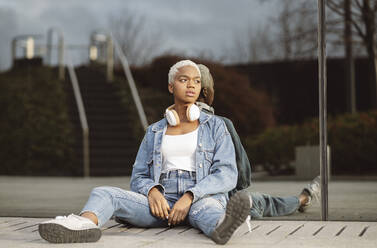 Thoughtful young woman looking away leaning on glass wall - JCCMF05130