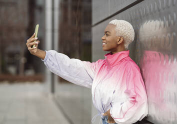 Junge Frau nimmt Selfie durch Smartphone vor der Wand - JCCMF05138